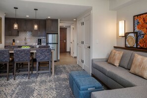 A modern kitchen with dark cabinets, a dining area with a blue upholstered bench, and a living room with a gray sofa. - Spacious 2BR Villa at Sheraton Steamboat\ Ski-In, Ski-Out \ Jan 4-9 (Steamboat Springs)