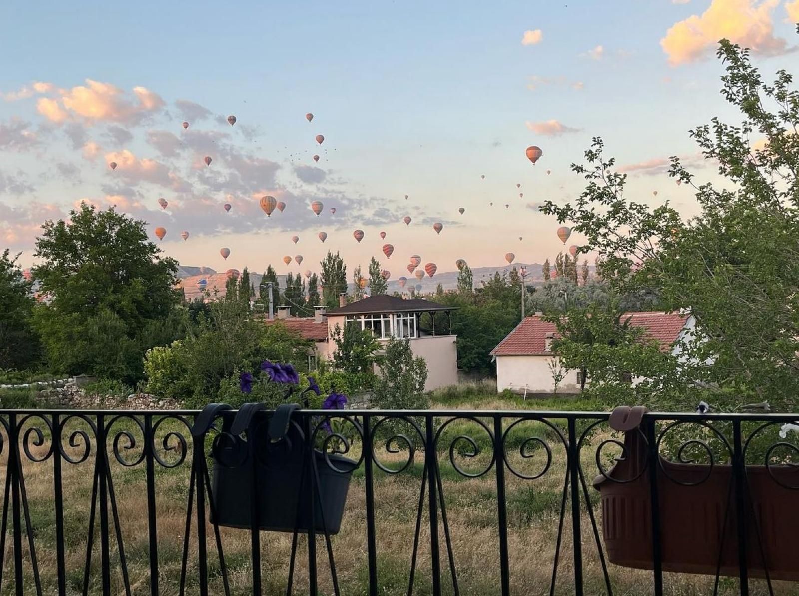 A balcony with a view of a village and hot air balloons in the distance.