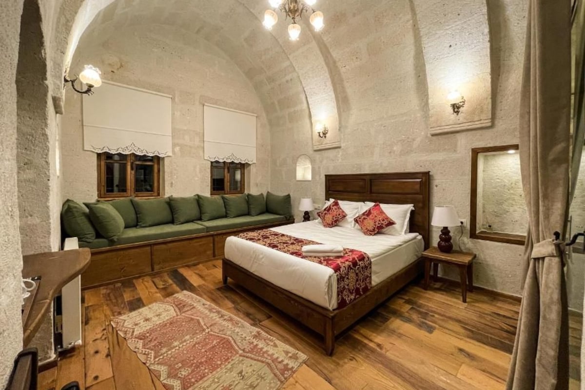 Habitació amb un llit gran, un sofà, terra de fusta i sostre de pedra.