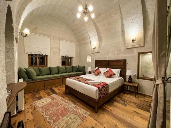A room with a large bed, a sofa, a wooden floor, and a stone ceiling. - Kemerli House (Avanos)