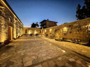Une cour dallée de pierres, avec des murs en pierre et un bâtiment doté de nombreuses fenêtres.