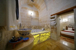 Un bany amb un lavabo de marbre, una banyera i un llit amb un capçal de fusta.