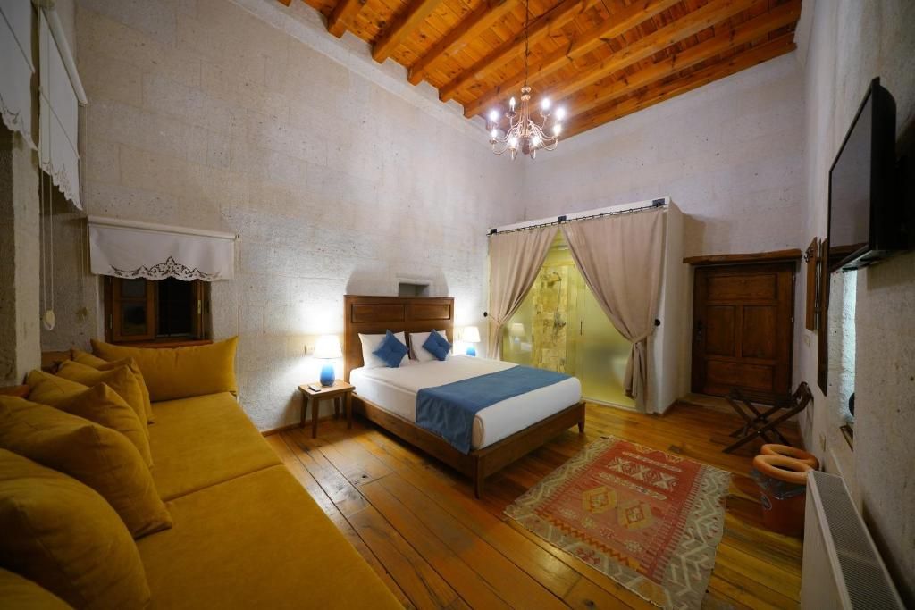Une chambre avec un plafond en bois, un lit recouvert d’une couverture bleue, une table de chevet en bois et un tapis à motifs.