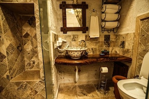 A bathroom with a marble-tiled wall, a wooden countertop, a white sink with a polka-dotted basin, a towel rack with towels, and a toilet.