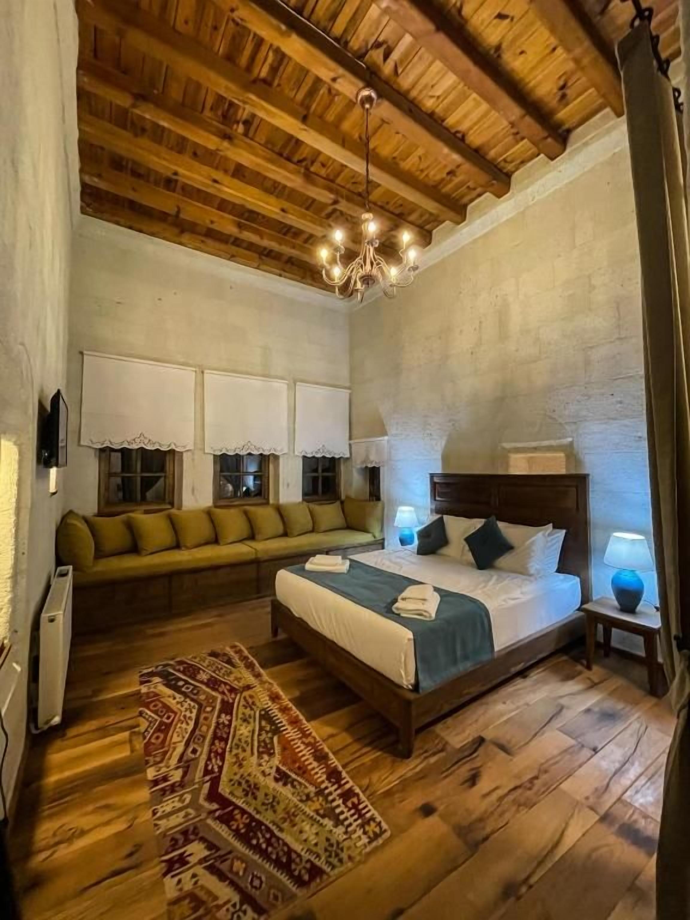 Une chambre avec un plafond en bois, un lit recouvert d’une courtepointe bleue, un canapé vert et un tapis à motifs.