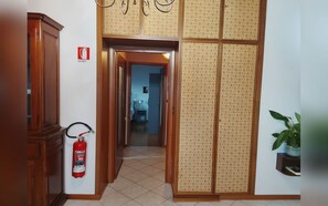 A hallway with a fire extinguisher mounted on the wall, a wooden cabinet, and a potted plant. - Family-friendly apartment that welcomes pets, just 45 minutes from Bologna and Florence. (Baragazza)