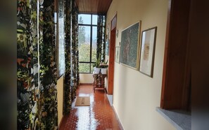 Um corredor com cortinas estampadas, tapete de boas-vindas, obras de arte emolduradas e vista para árvores pela janela.