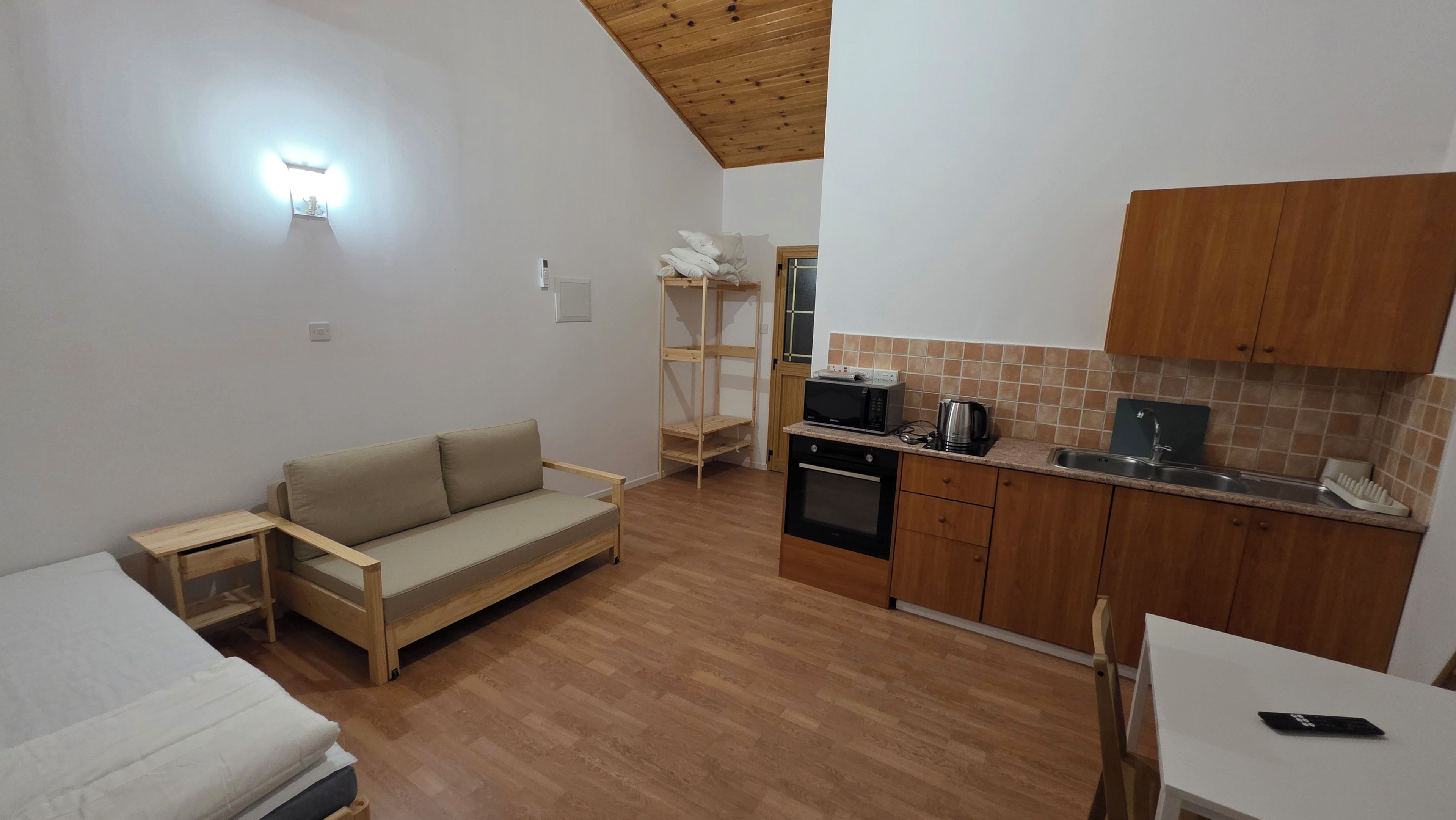 A compact kitchen with a wooden ceiling, a sofa, a dining table, and a microwave.
