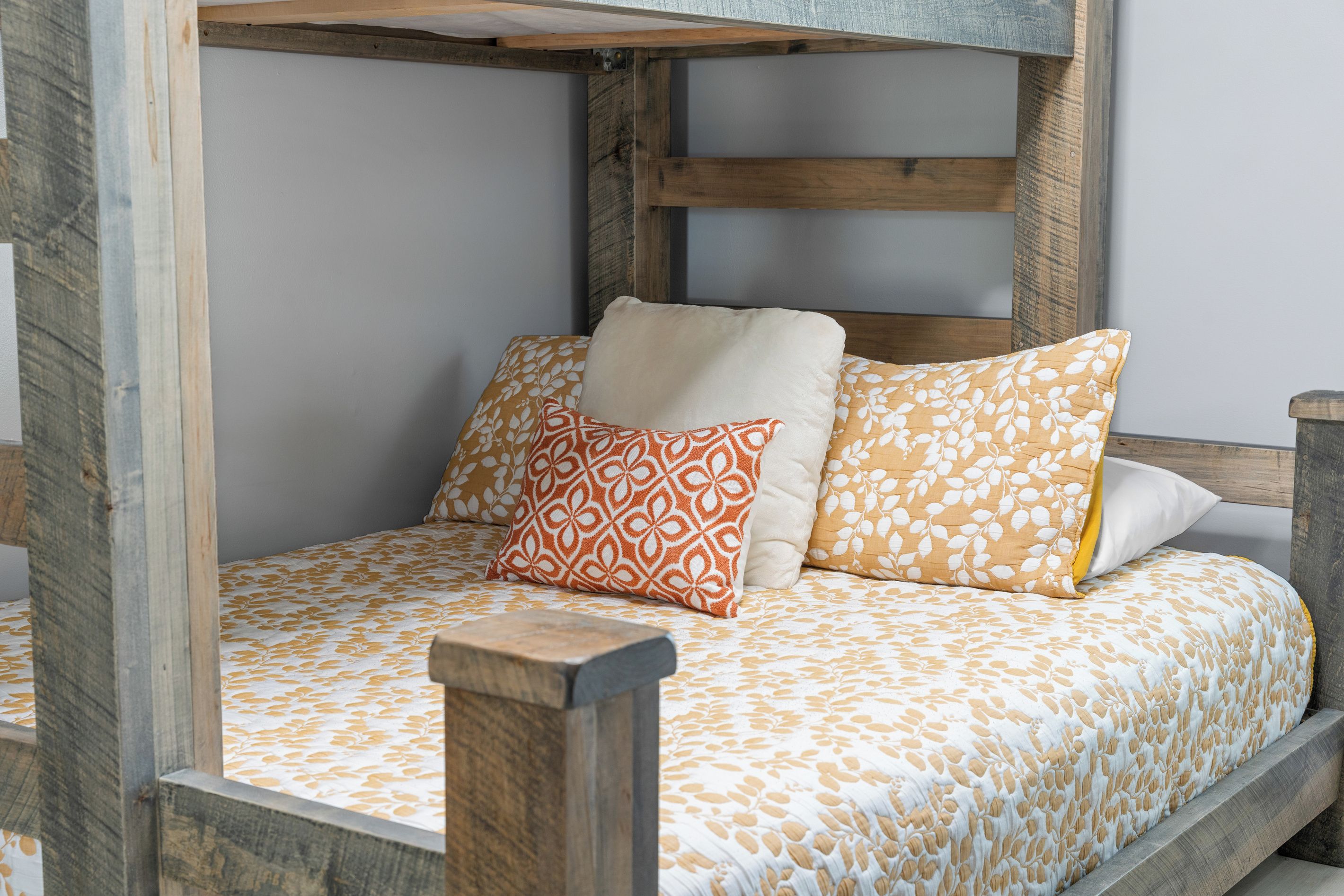Ein Bett mit einem gemusterten Überwurf, zwei Kissen mit Blättermotiv und einem hölzernen Kopfteil.