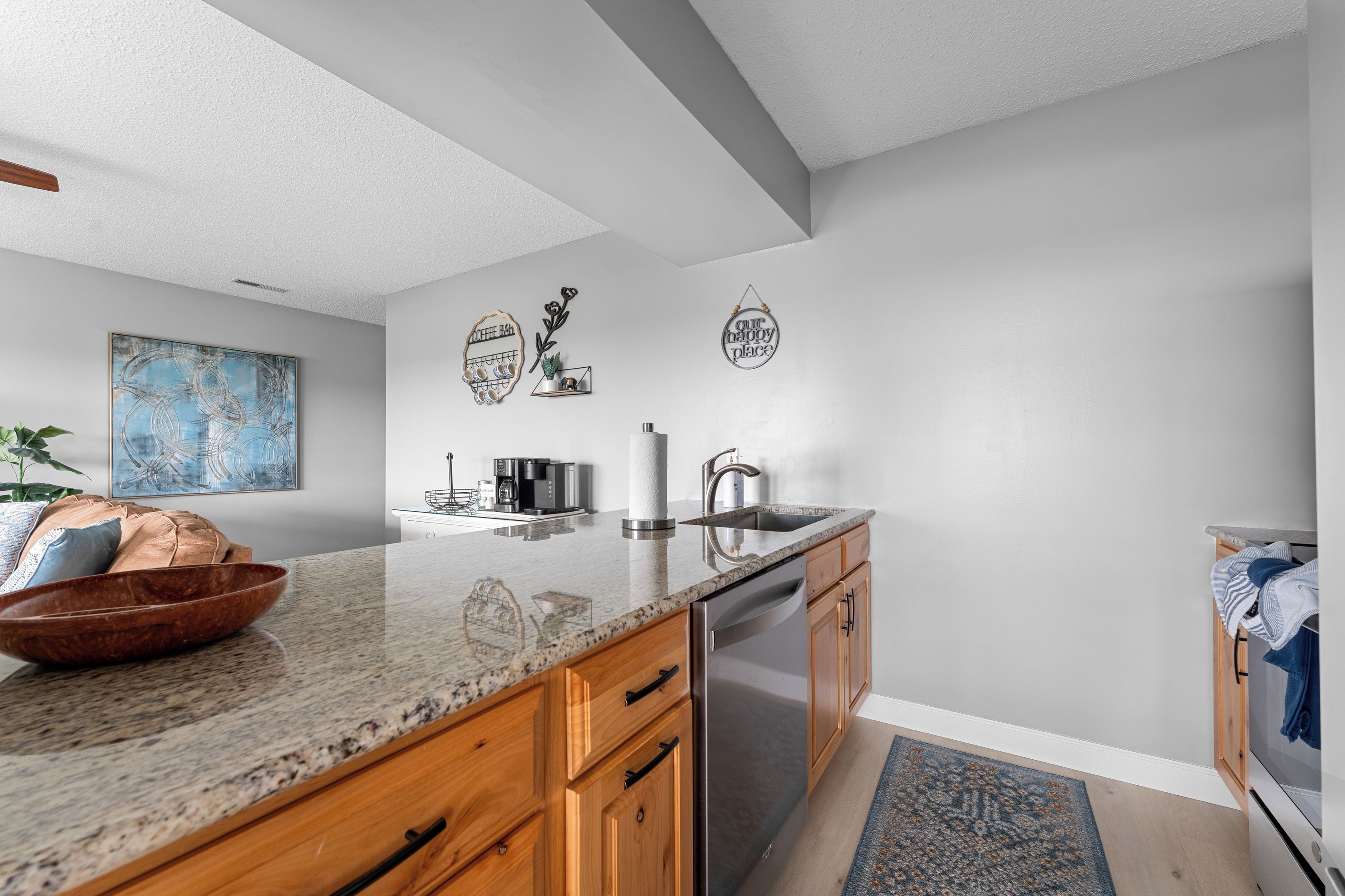 A modern kitchen with a granite countertop, stainless steel appliances, wooden cabinets, and decorative wall art.