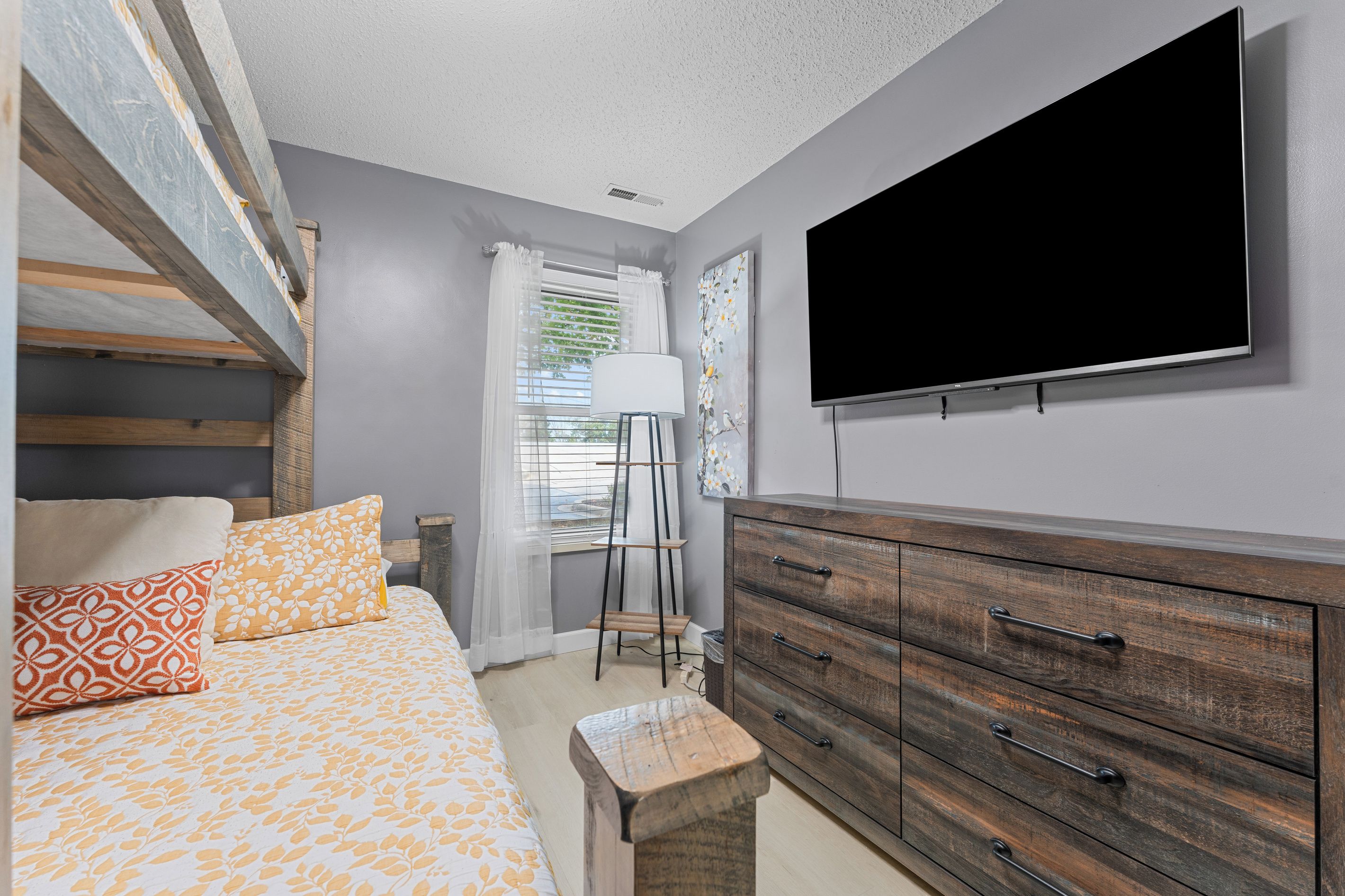 A bedroom with a bed, a dresser, a TV, and a window with curtains.