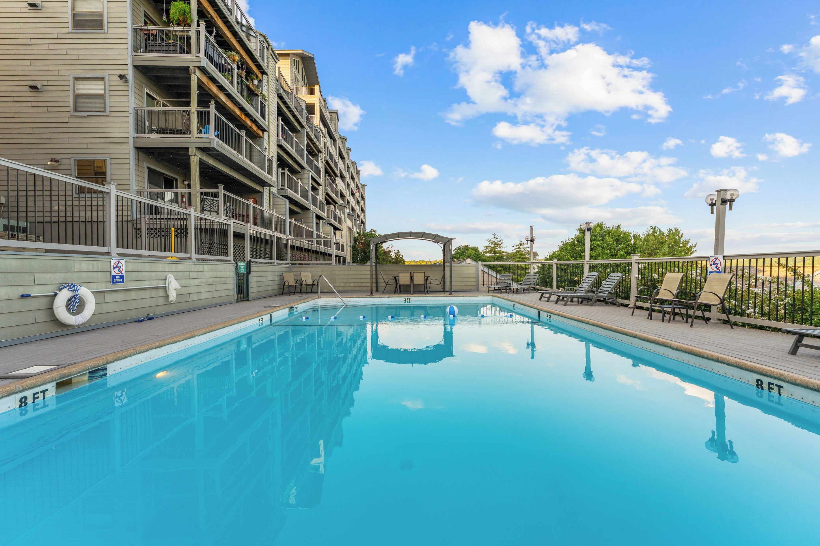 A swimming pool with a clear blue water surface, surrounded by a wooden deck with lounge chairs.