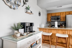 A modern kitchen with wooden cabinets, a coffee station, and a glass-top dining table with two bar stools. - Huge Table Rock Lake Views, Sleeps 5- Close to SDC (Branson)