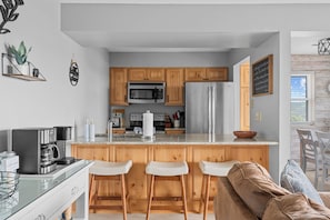 Eine moderne Küche mit Holzschränken, einem Edelstahlkühlschrank, einer eingebauten Mikrowelle und einer Kaffeemaschine.