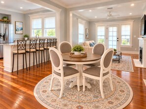 A dining area with a round table and chairs, a kitchen in the background, and a patterned rug on the floor. - The Biloxi Muse on Lameuse St. (Biloxi)