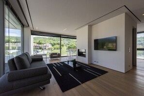 A modern living room with a large TV, a sofa, and a view of a green landscape through large windows. - Villa Bilor Luxe 6 by MMega (Subbiano)