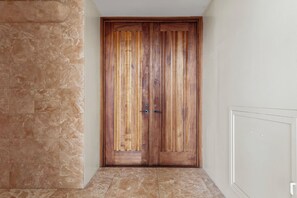Una porta doble de fusta amb disseny de panells verticals, situada en un passadís amb paviment de pedra i una paret sense decoració.