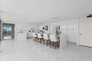 A modern kitchen with white cabinetry, a marble countertop, and a dining area with four chairs. - Luxury 2-Story Penthouse - Diamond Head & Ocean Views - Private Jacuzzi (Honolulu)