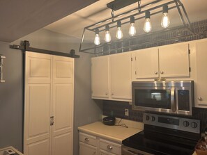 A kitchen with white cabinets, a black stove, a microwave, and a light fixture with exposed bulbs. - Lake front Cozy 2-bedroom, 2-bath condo with AC in wonderful Port Clinton (Port Clinton)