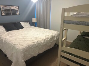 A hotel room with a bed, a bunk bed, a lamp, a window with curtains, and a wall-mounted picture. - Lake front Cozy 2-bedroom, 2-bath condo with AC in wonderful Port Clinton (Port Clinton)