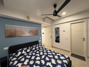 Ein Schlafzimmer mit einem Bett, einem Deckenventilator, einer Klimaanlage, einer Tür und einem wandmontierten Spiegel.