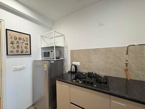 A compact kitchen with a gas stove, a microwave, and a refrigerator. - Finland - 1BHK_Hiranandani Estate_Thane (Thane)