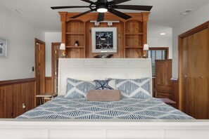A bedroom with a bed, wooden headboard, ceiling fan, and built-in shelving. - Oceanside, 5 Story, w/Tiki Bar, 4th Flr HotTub, Panoramic view of Ocean & Sound! (Avon)