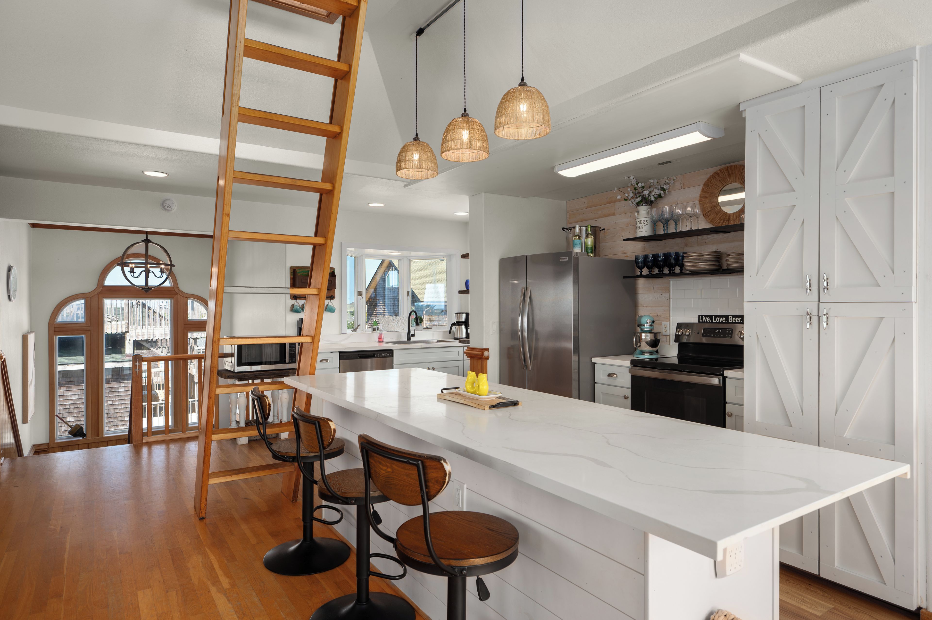 A modern kitchen with a central island, stainless steel appliances, and a wooden ladder.