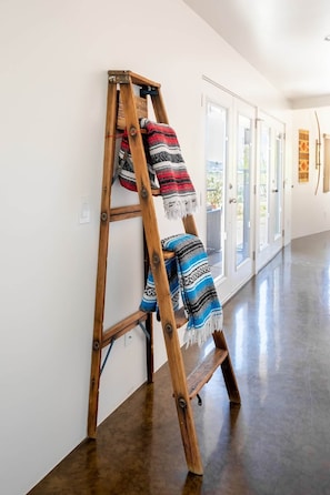 Una escalera de madera apoyada contra una pared blanca, con dos mantas colgadas.