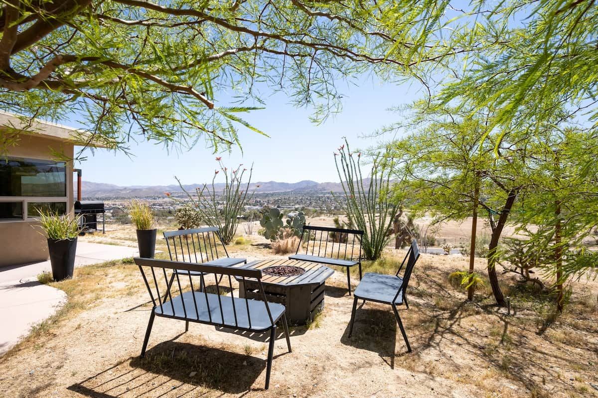 An outdoor seating area with a fire pit, surrounded by desert vegetation and a view of distant mountains.