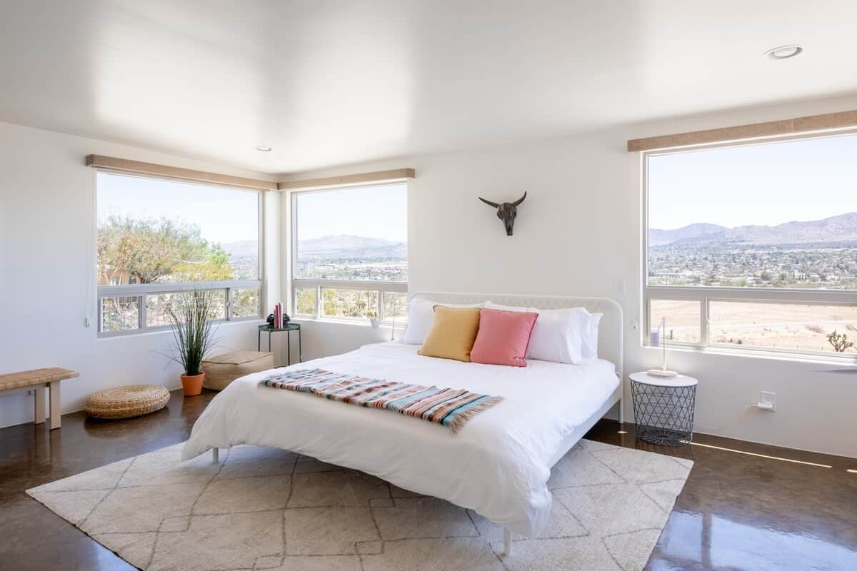 A bedroom with a large bed, a bull head decoration, a view of the desert, and a potted plant.