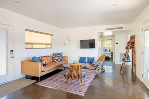 A modern living room with a sofa, a wooden chair, a television, and a patterned rug. - Natural Modern • 180deg Views • Hot/Cool Tub • Near Pappy and Harriet's (Yucca Valley)