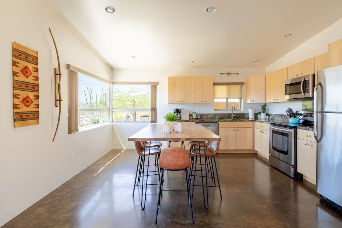 A modern kitchen with a dining area, large windows, and a view of the outdoors.