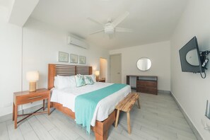 A bedroom with a bed, bedside tables, a desk, a chair, a ceiling fan, and a TV mounted on the wall. - Amazing Beachfront Villa w Chef Maid at Cabarete (Sosúa)