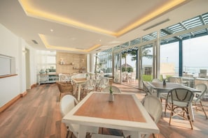 Un espace repas moderne avec une table et des chaises en bois, une cuisine en arrière-plan et de grandes fenêtres offrant une vue sur la plage.