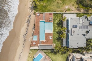 A beachfront property with a large swimming pool, a separate pool area, and a building with solar panels. - Amazing Beachfront Villa w Chef Maid at Cabarete (Sosúa)