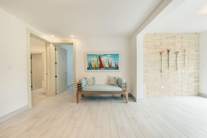 A modern living room with a wooden bench, a painting of sailboats, and a brick wall with decorative elements. - Amazing Beachfront Villa w Chef Maid at Cabarete (Sosúa)