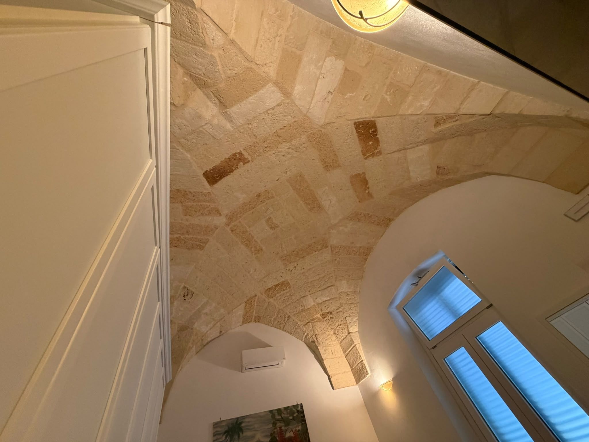 A high-ceilinged room with stone walls, a skylight, and a painting.