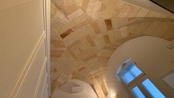 A high-ceilinged room with stone walls, a skylight, and a painting.