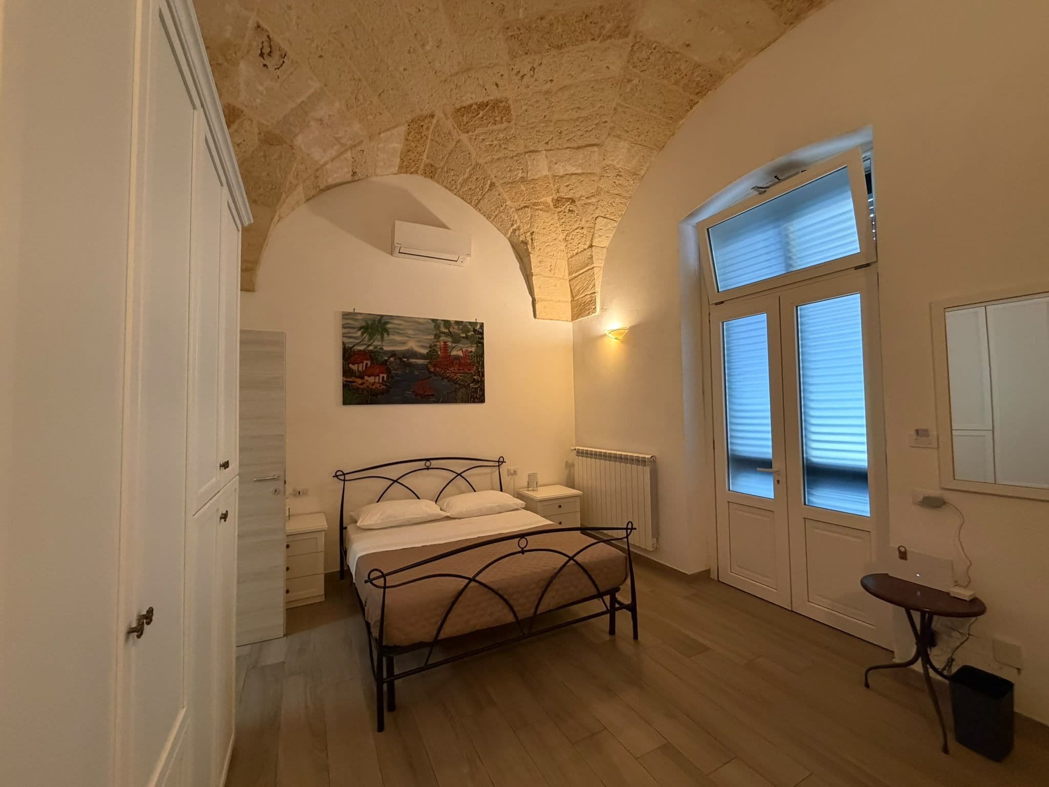 A bedroom with a bed, a nightstand, a radiator, and a window with blinds.
