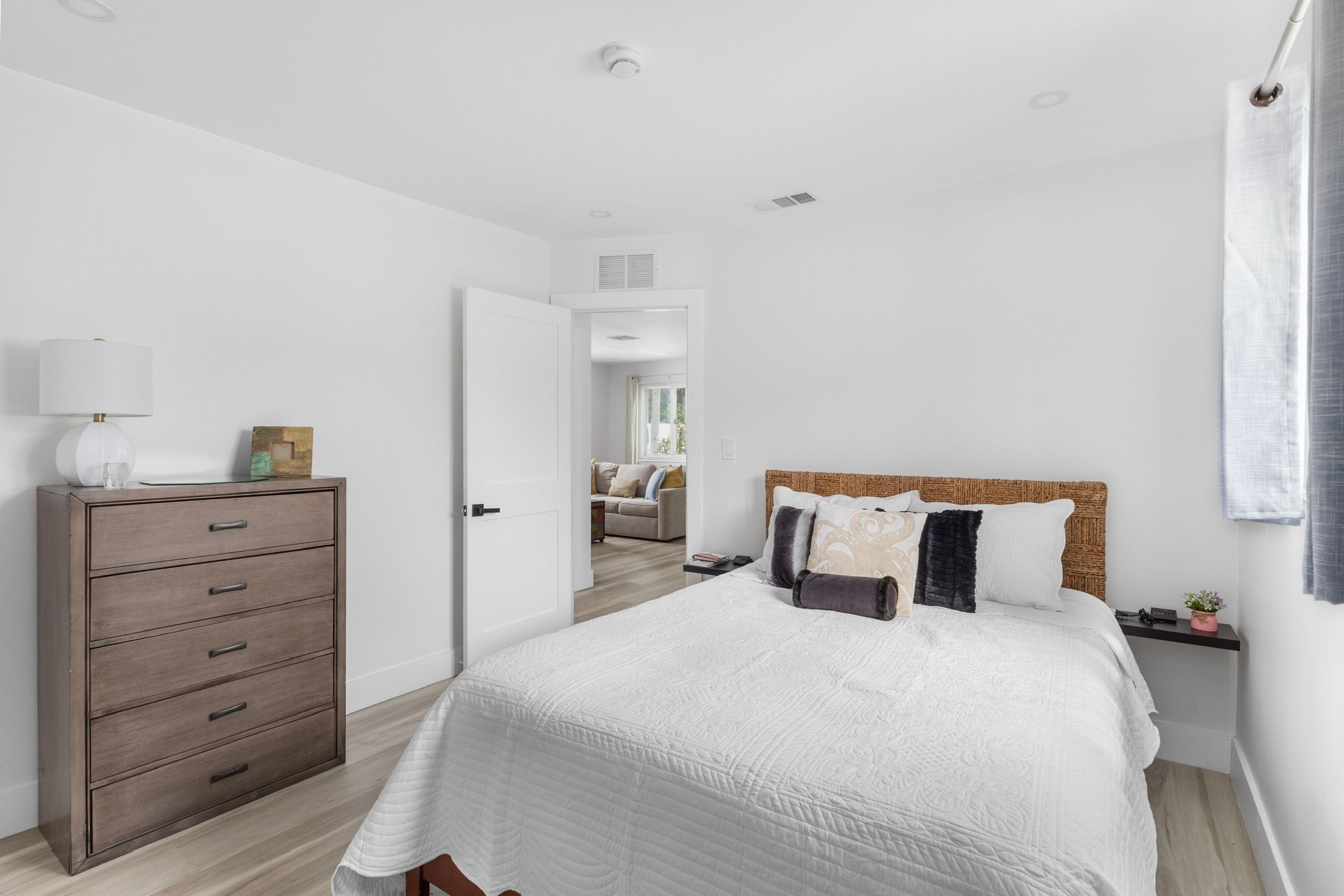 A bedroom with a bed, a dresser, a nightstand, and a door leading to another room.