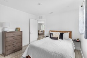 Un dormitorio con cama, cómoda, mesita de noche y una puerta que da a otra habitación.
