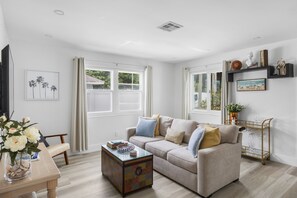 A living room with a beige sofa, a coffee table, a TV, and a bookshelf. - Two bedroom house in quaint Dania Beach on a canal and next to airport (Dania Beach)