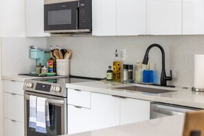 Una cocina moderna con horno de acero inoxidable, microondas, lavabo con grifo negro y varios utensilios de cocina sobre la encimera.