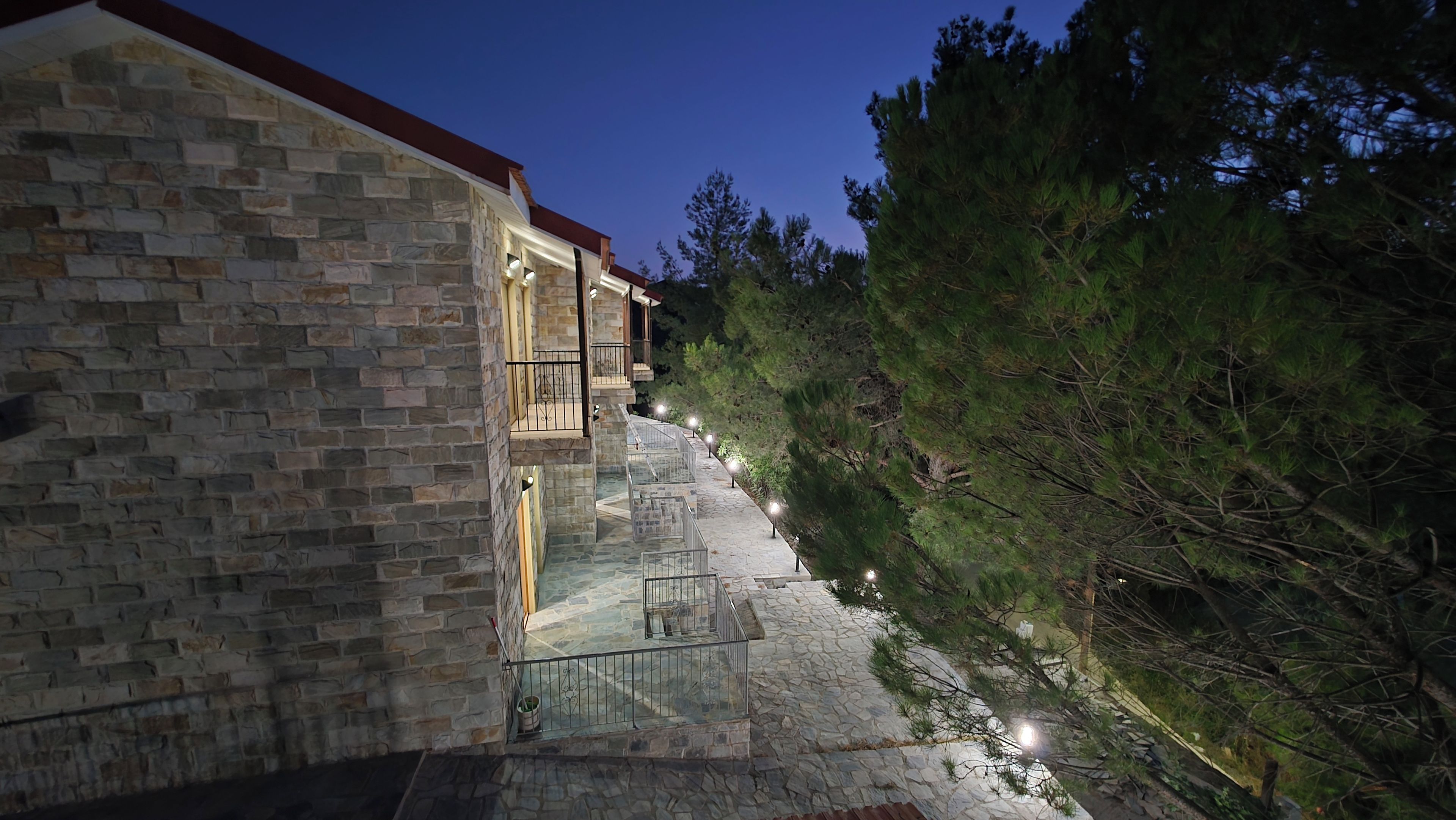 A stone building with a balcony, surrounded by trees and a stone pathway.