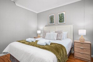 A neatly made bed with white linens and a green throw blanket, a bedside table with a lamp, and a nightstand with a lamp. - Azure 119 - Two Bedroom Apartment, Sleeps 4 (Cape Town)
