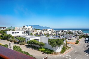 A coastal residential area with modern buildings, a parking lot, and a view of the ocean. - Azure 119 - Two Bedroom Apartment, Sleeps 4 (Cape Town)