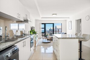 A modern kitchen with a view of the city, a dining area with a view, and a large window. - Azure 119 - Two Bedroom Apartment, Sleeps 4 (Cape Town)
