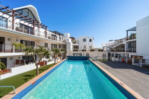 Piscina com superfície de água azul cristalina, rodeada por edifícios modernos com varandas e guarda-corpos.