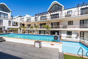 A modern hotel with a pool area, multiple balconies, and a clear blue sky. - Azure 119 - Two Bedroom Apartment, Sleeps 4 (Cape Town)